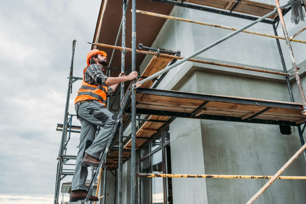 handsome builder climbing on scaffolding at construction site